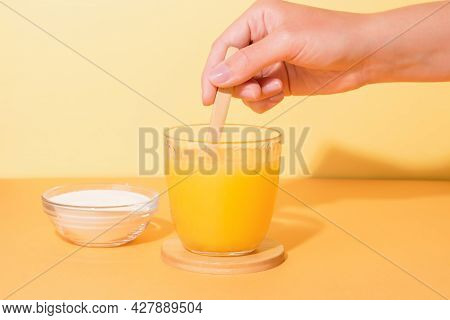 Orange Juice Glass And Collagen Powder On Table With Plant In Hard Light. Bright, Minimal Compositio