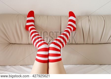 Female Legs In Knee Socks With Red And White Stripes On A Bed. Concept Of Christmas Celebration, Pla