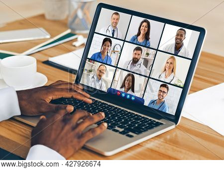 Black Doctor At Laptop Having Video Conference With Colleagues Indoor
