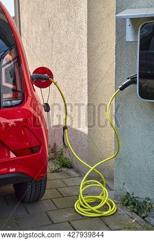 A Red Electric Car Is Charged Via A Cable.