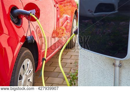 A Red Electric Car Is Charged Via A Cable.