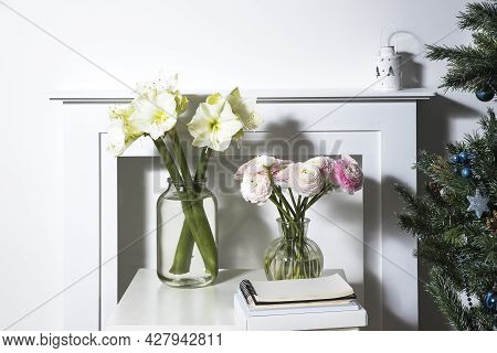 A Bouquet Of Pink Persian Buttercups In A Glass Vase And Two Wrapped Gifts On A White Table In Front