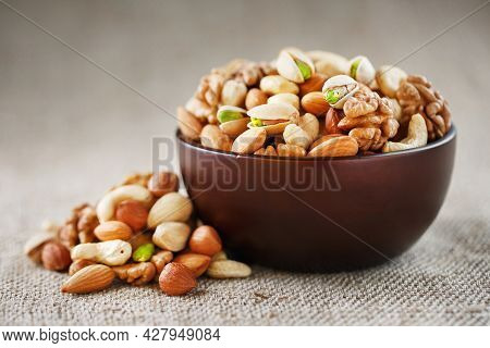 Nuts Of Various Varieties Spill Out From A Wooden Plate On A Table With A Burlap Cloth.