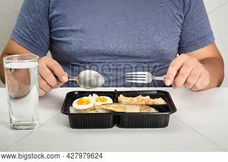 Fat Man Eating A Box Of Food On A White Table. Concept Of Home Quarantine For Covid-19 Patients Asym