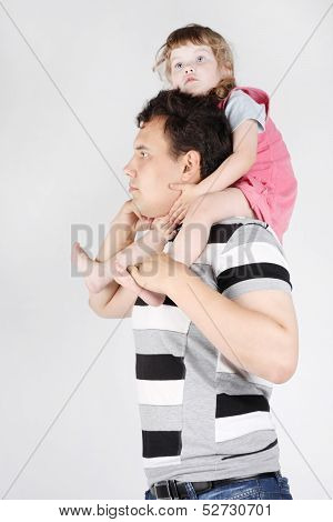 Little Girl Sits On Shoulders Of Her Father And Dreams On Grey Background.