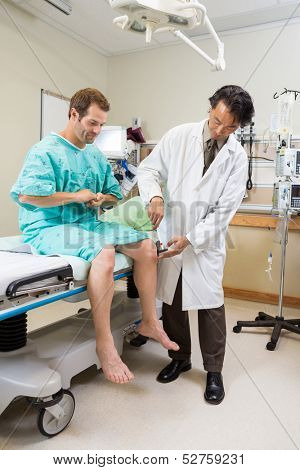 Full length of male doctor examining patient's knee with hammer in hospital room