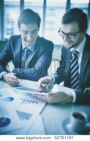 Image of two young businessmen discussing document in touchpad at meeting