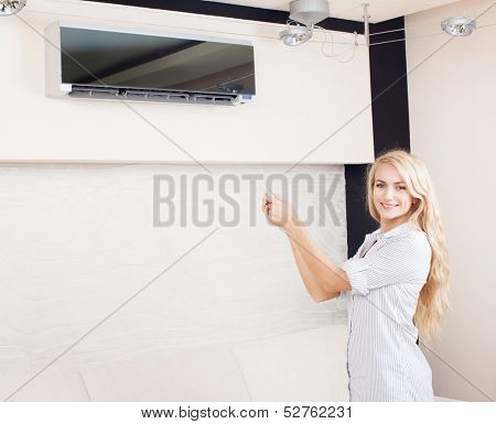Female holding a remote control air conditioner at home. Happy young woman on sofa