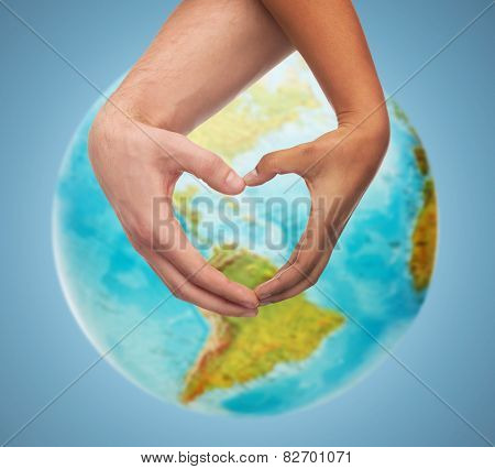 people, peace, love, life and environmental concept - close up of human hands showing heart shape gesture over earth globe and blue background