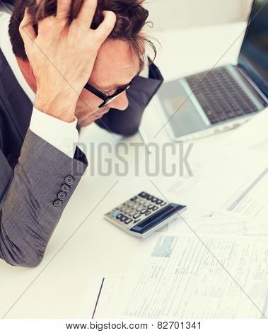 tax, business and stress concept - stressed businessman with papres, laptop and calculator