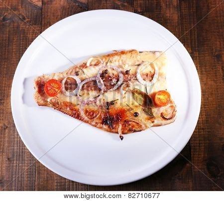 Dish of Pangasius fillet with spices and vegetables on plate and wooden table background