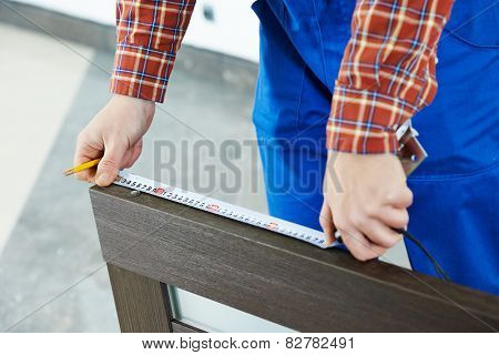 Close-up carpenter hands with measure tape during process of wood door installation 