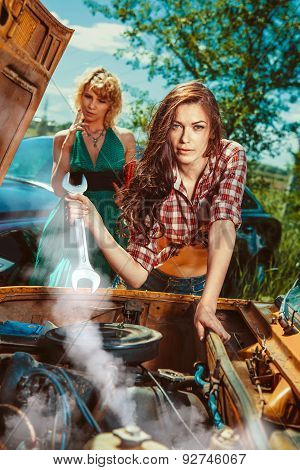 Woman Mecanic Is Repairing A Car Another Woman Is Smoking On The Background.
