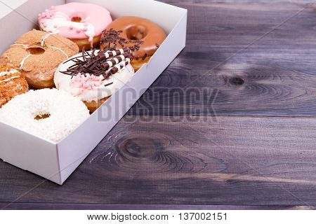 Delicious donuts with colorful glaze and sprinkles in a box on a dark wooden background.