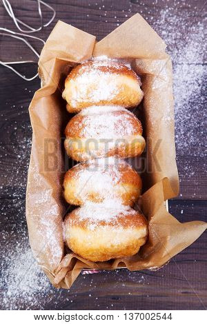 German donuts - berliner with jam and icing sugar in a box on a dark wooden background. Top view