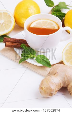 Cup of tea with lemon mint cinnamon and ginger on a white wooden table