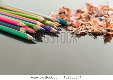 Sharpened colorful pencils and pile of colorful pencil shavings on black glass gloss table with shallow depth of focus