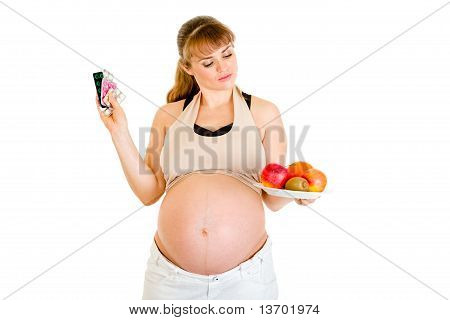 物思いにふけるの妊娠中の女性の丸薬と白で隔離の果物の間の選択を行う