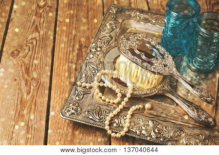 Vintage hand mirror and hairbrush on silver tray over wooden background