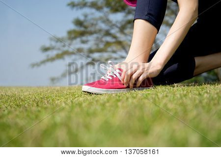 Running shoes - closeup of woman tying shoe laces on her barefoot running shoes. Female sport fitness runner getting ready for jogging outdoors.
