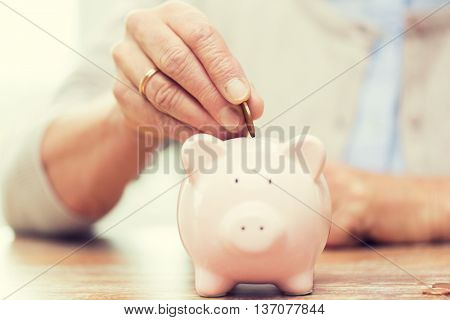 savings, money, annuity insurance, retirement and people concept - close up of senior woman hand putting coin into piggy bank