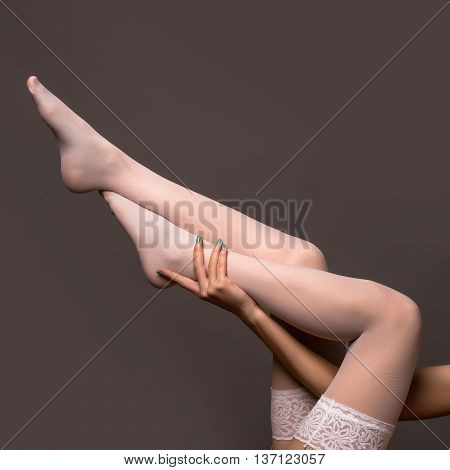 female long legs of young pretty woman with sexy slim body in erotic white color stockings on grey background copy space