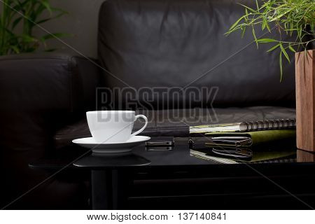 white coffee cup on glass table with dark brown sofa in living room