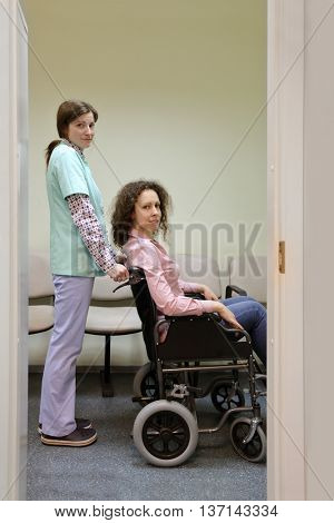 nurse and patient in chair wheelchair in hospital corridor, looking at camera