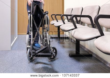 woman folds or unfolds black wheelchair in lobby of hospital