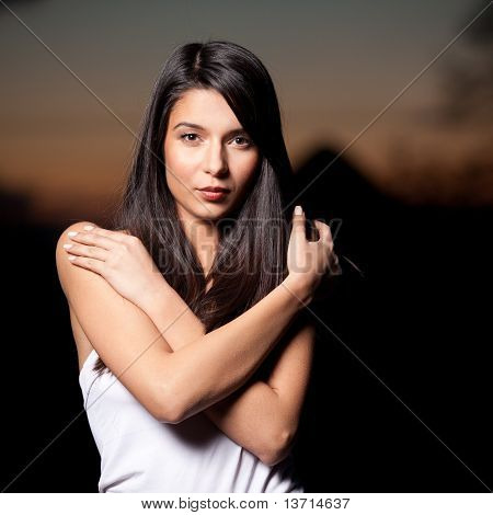 Un retrato de una mujer joven al atardecer, con los brazos alrededor de sus hombros