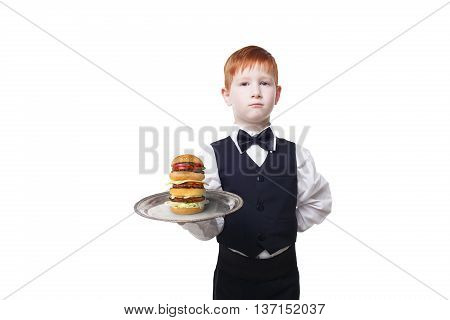 Little waiter stands with tray serving big double hamburger. Redhead Child boy in suit plays restaurant servant, gives burger isolated at white background