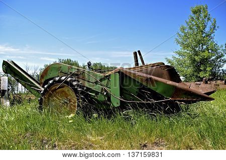 An old mounted green corn picker is mounted on the front end of a a tractor