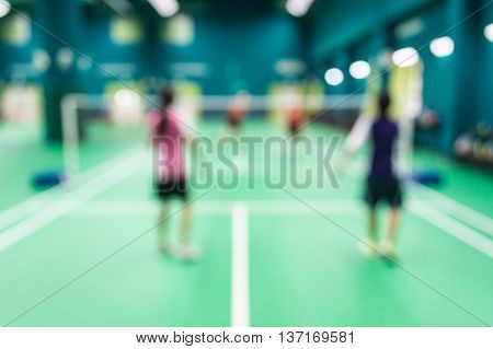 Blurred people playing badminton in green court.