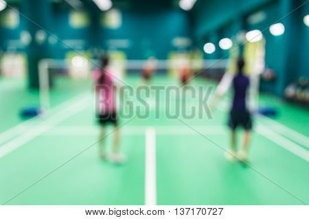 Blurred people playing badminton in green court.