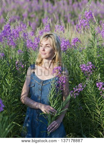 The smiling young woman with bunch of willowherb flower in the field