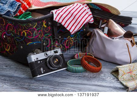 Camera near suitcase with clothes. Colorful striped bracelets. Vintage camera on gray shelf. Take some pictures during journey.