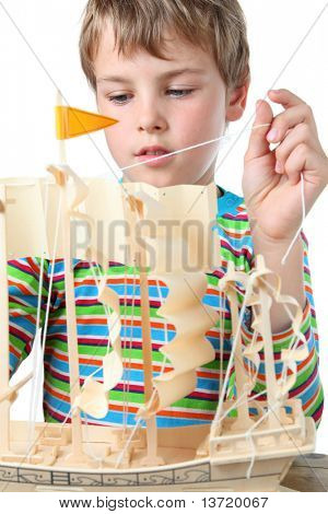 Small boy in striped shirt works with zeal on artificial ship, he pulls the sail