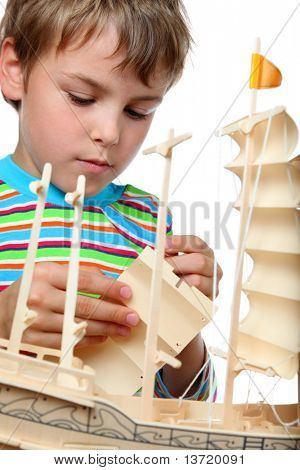 Small boy in striped shirt works with zeal on artificial ship, he makes sails