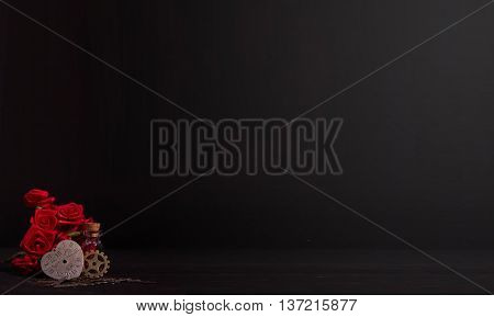 timeless heart next to the red ribbon roses, a cog wheel and glass bottle in the dark