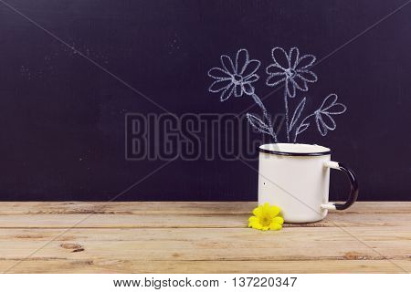 Coffee cup on wooden table over chalkboard background with hand drawing flowers.