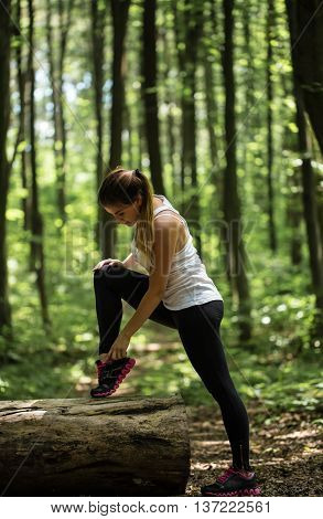 sporty girl in the woods is warming up near a big log sport