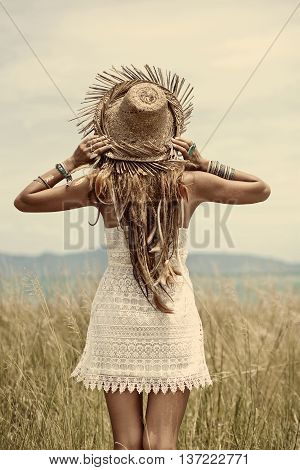 Attractive boho style woman in straw hat. Back view