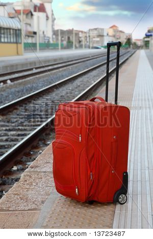 große rote Reisetasche steht auf Plattform in der Nähe von Gleisanlagen. Perspektive