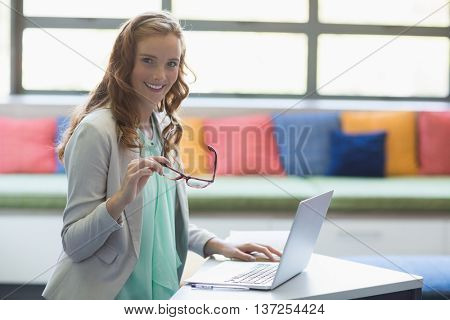 Portrait of smiling teacher using laptop in library