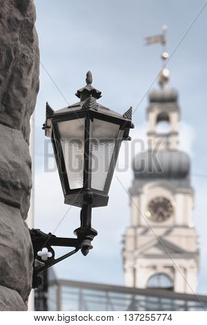 Street lamp on the facade of an old house in the background the tower of City Hall in Riga with a clock and weather vane