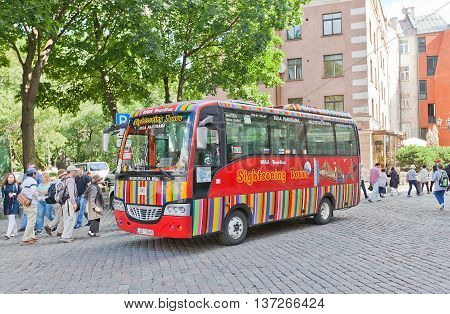 RIGA LATVIA - JULY 05 2016: Red city sightseeing bus waiting for tourists near Church of St Peter in Riga Latvia. Povides excursion tours around old Riga (UNESCO site)