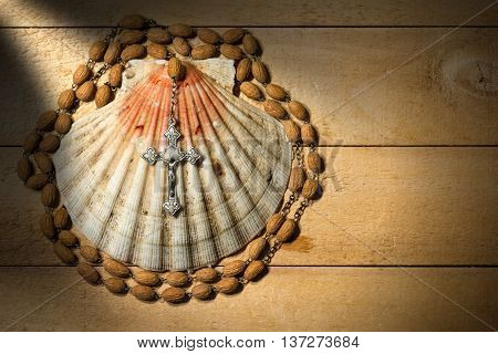 Scallop seashell and wooden rosary beads with a silver crucifix on a wooden background. Symbols of Christian pilgrimage