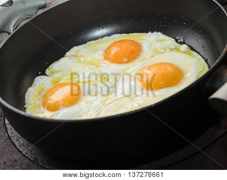Three fried eggs in a black frying pan
