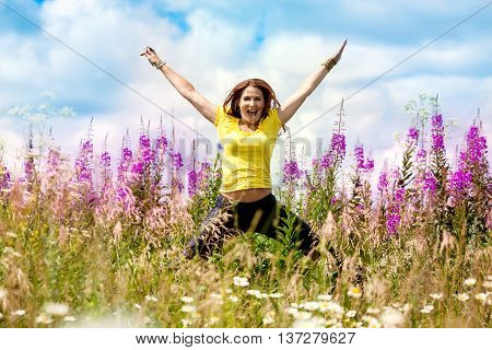 Young happy girl in the field with lilac flowers in a jump
