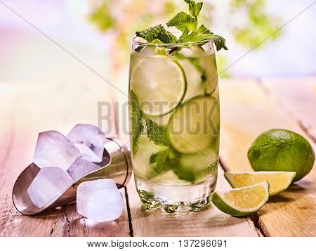 Alcohol drink. On wooden boards is glass with alcohol drink and ice cubes. A drink number thirty four cocktail mohito and scoop ice . Country life cocktail . Outdoor. Light background.